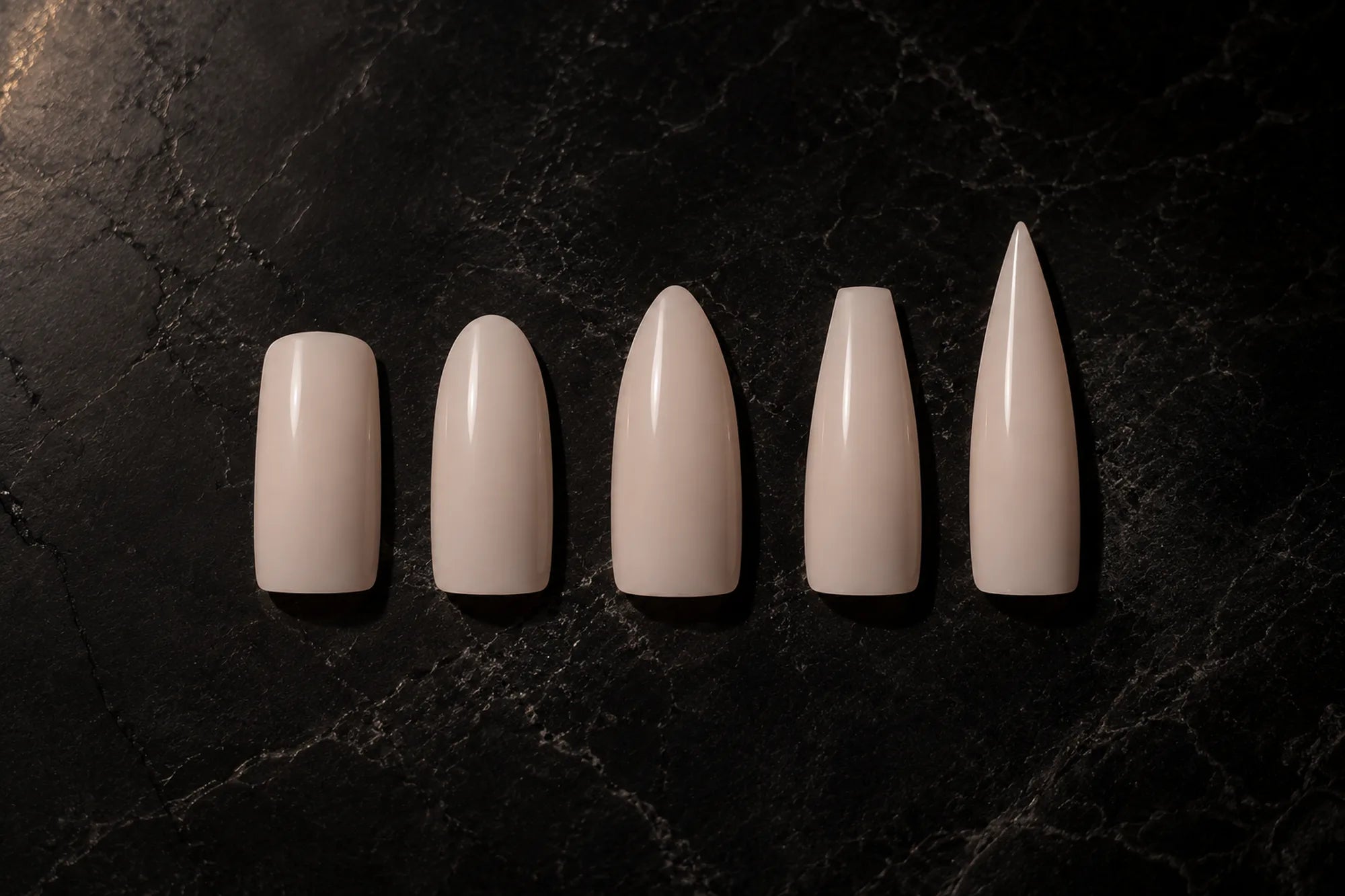Five press-on nail shapes from square to stiletto on dark marble