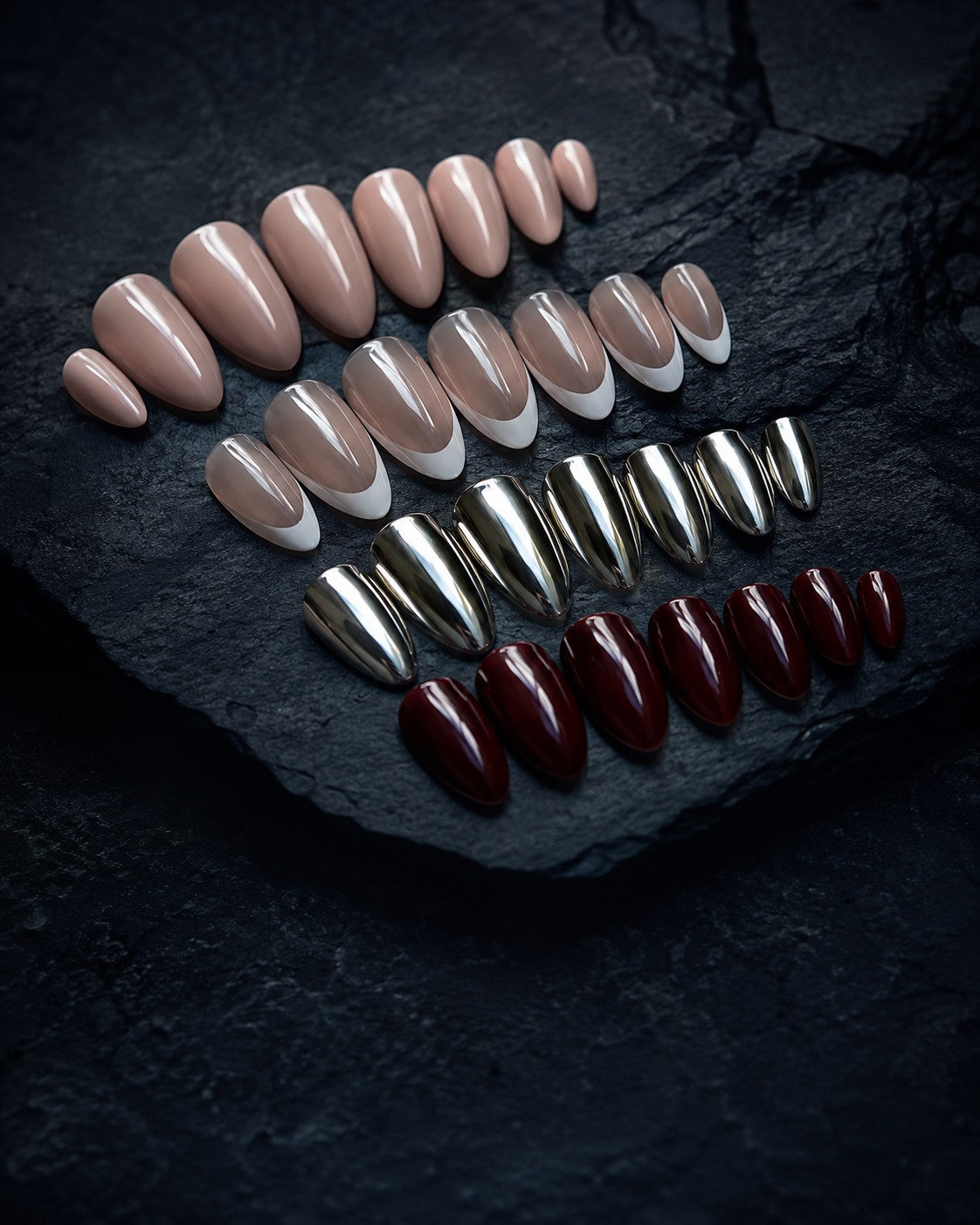 Four best selling press-on nail sets fanned on dark polished stone: nude almond, white French, mirror chrome and burgundy