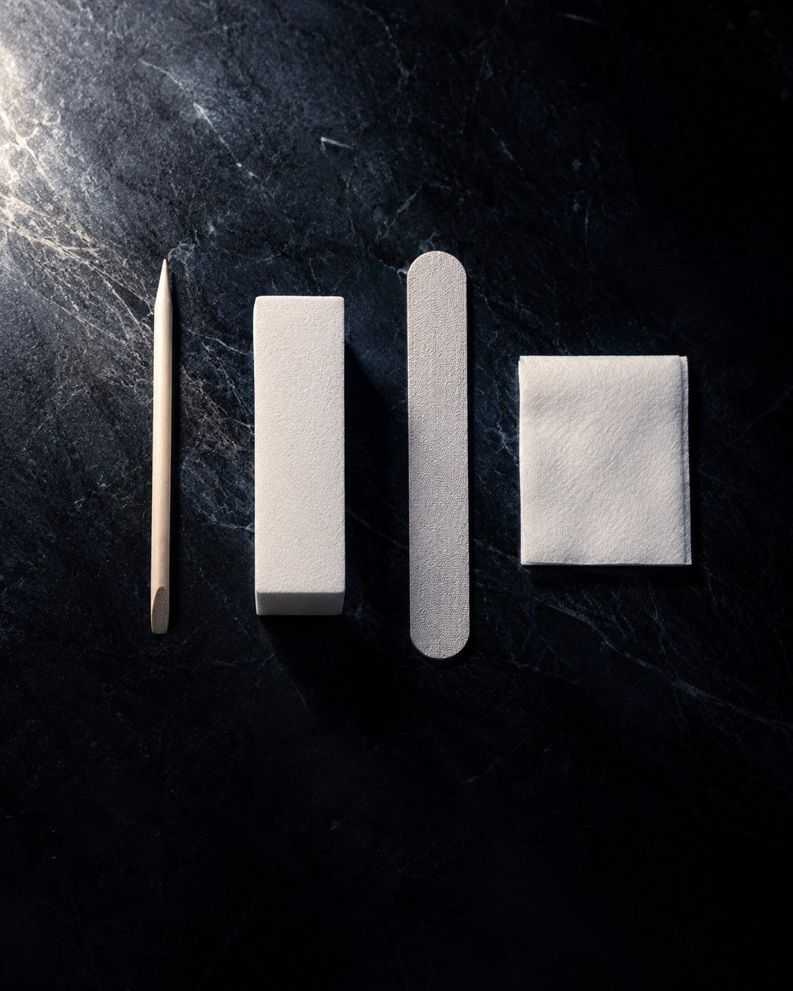 Press-on nail prep tools laid out in a row: cuticle pusher, buffing block, file and prep pad