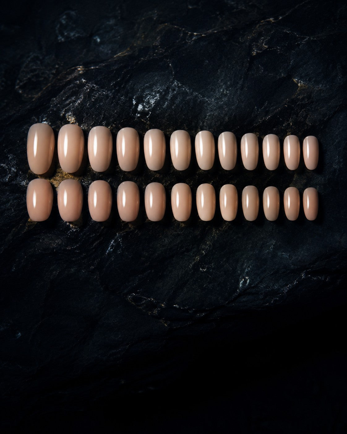A full set of bare milky nude press-on nails laid out by size on dark polished stone