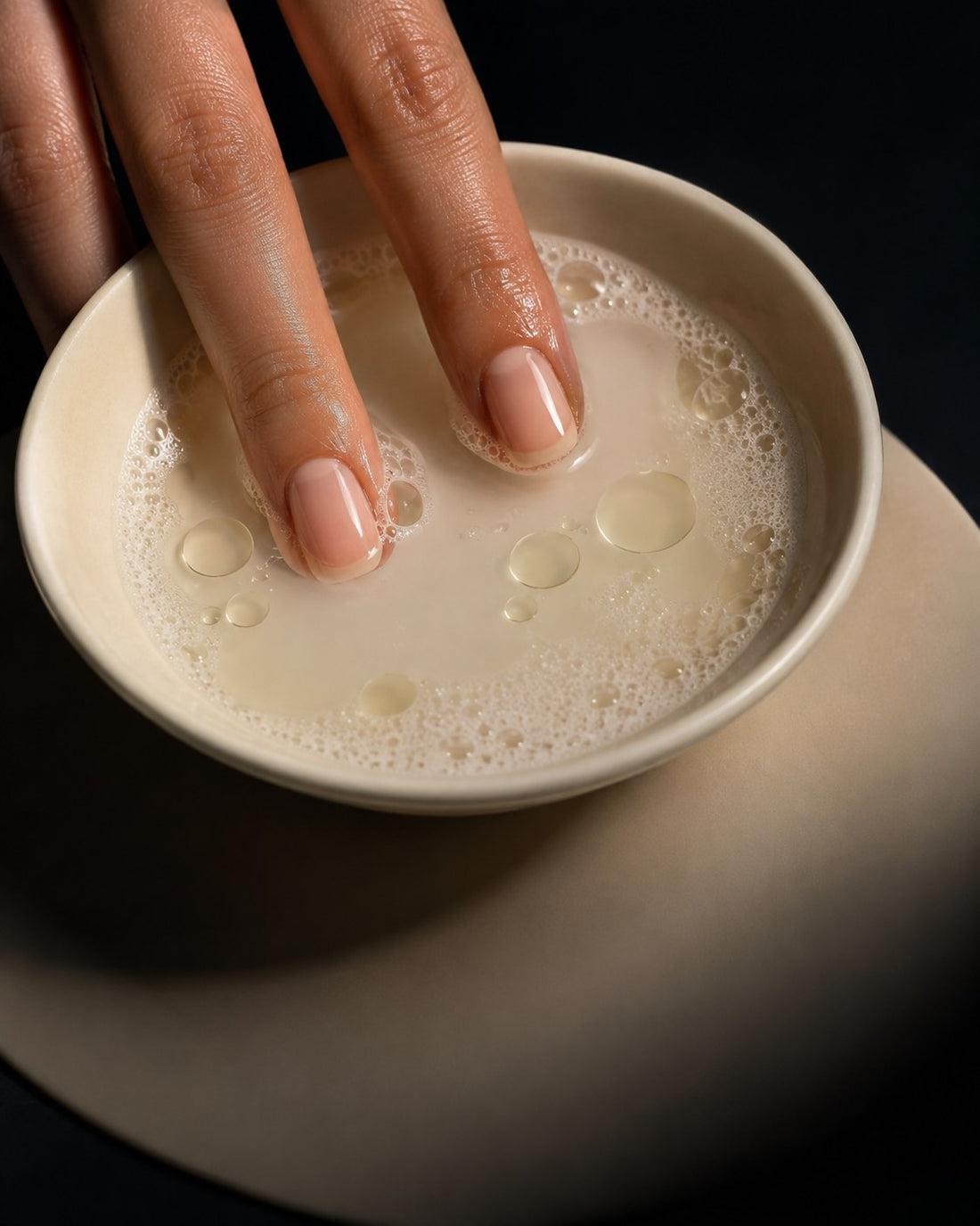 Fingertips soaking in a bowl of warm soapy water with a few drops of oil, the damage free removal