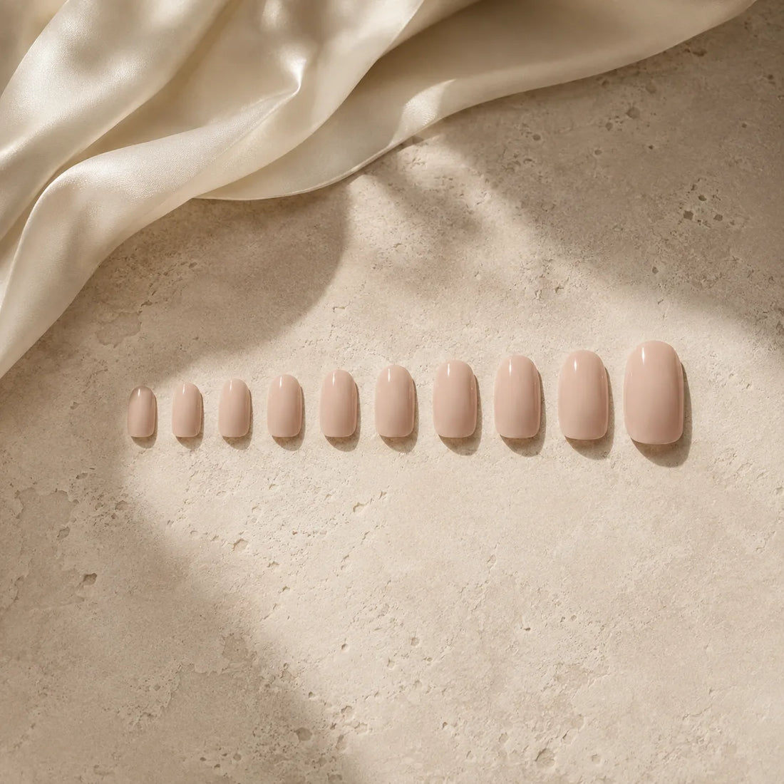 Twelve press-on nail sizes in a row on ivory travertine, Hands Down sizing